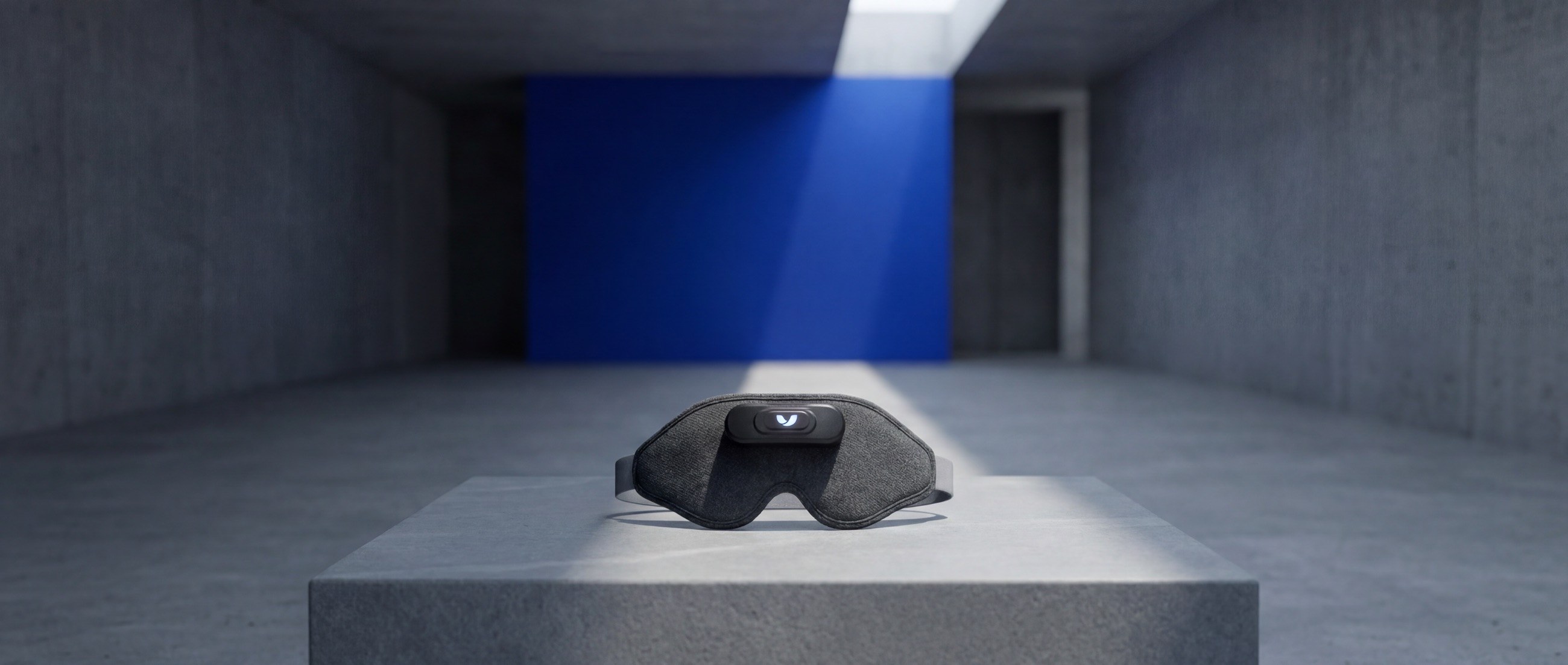 The Mask resting on a stone plinth under a shaft of light against a cobalt wall